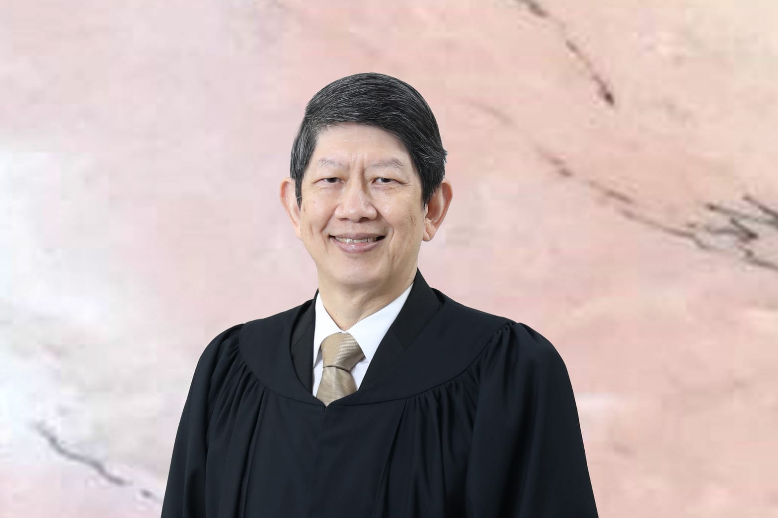 Smiling man in black judicial robe and tie against marbled background.